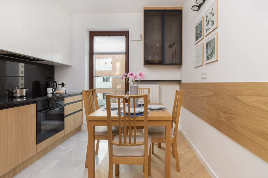 A compact kitchen with wooden cabinets and a dining table set for two. The design is practical and modern.