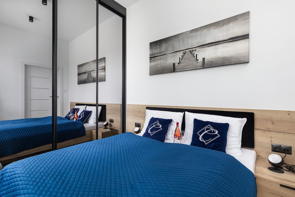 A bedroom with a blue bedspread, decorative pillows, and framed artwork above the bed.