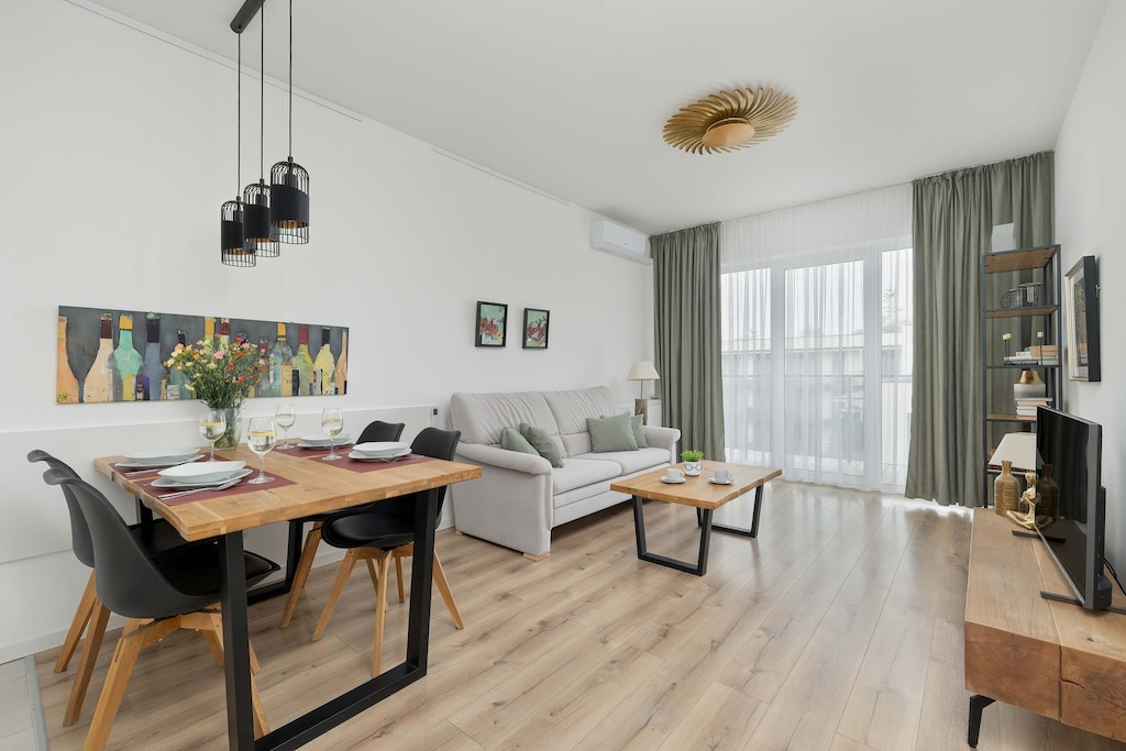 A bright and modern living room with a cozy sofa, flat-screen TV, and large windows bringing in natural light.