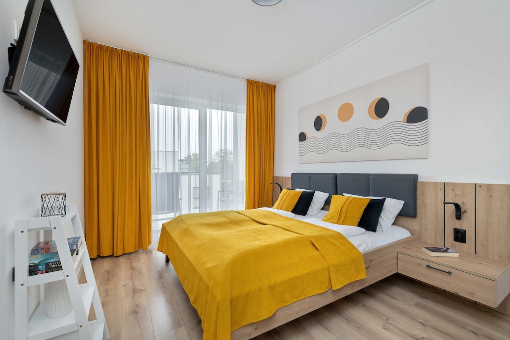 A cosy bright bedroom with yellow accents and a wall hanging for evening entertainment.