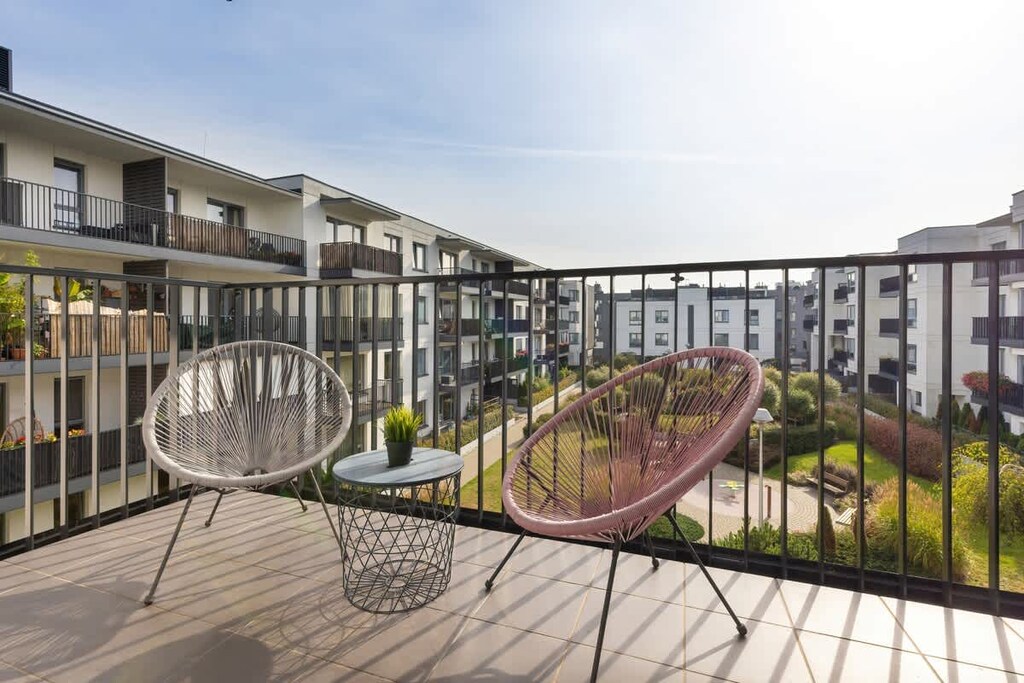 A spacious balcony with two round chairs, offering a view of the modern courtyard below.
