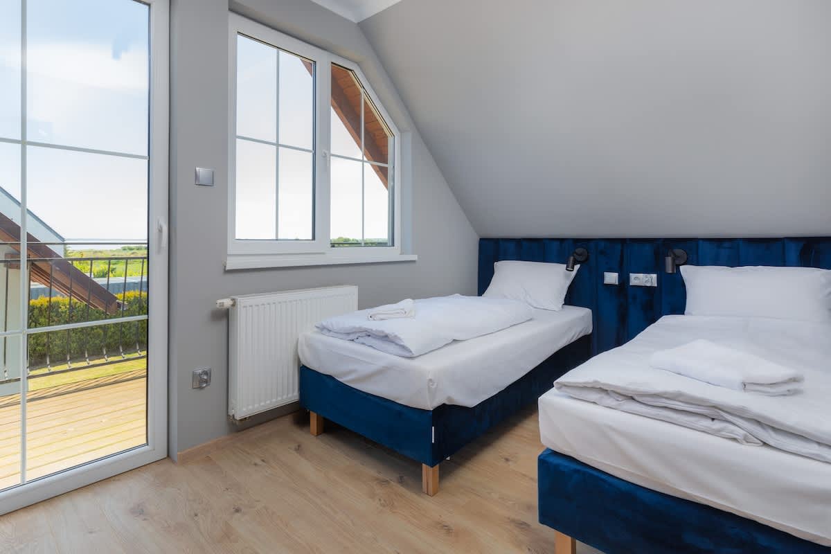 Another angle of a bedroom with two single beds under a slanted ceiling, offering a bright and airy feel with large windows providing natural light.