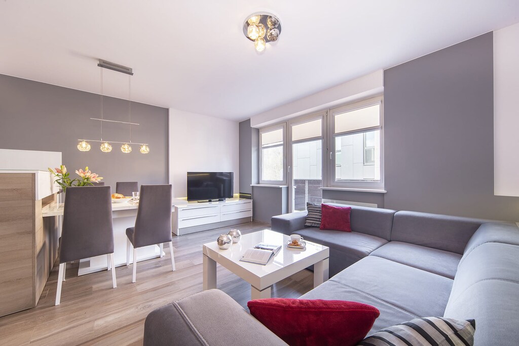 A bright and cozy living room with a comfortable gray sectional sofa, a coffee table, and windows offering a view of the outdoors.