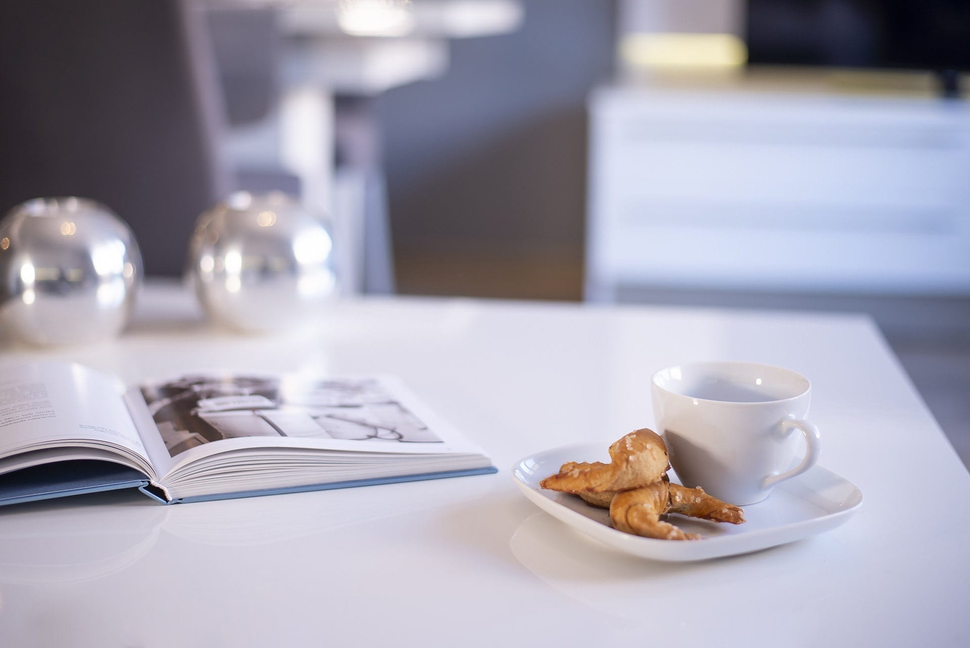 A close-up of a breakfast table setup, showcasing coffee cups, pastries, and a magazine for acoy morning vibe.