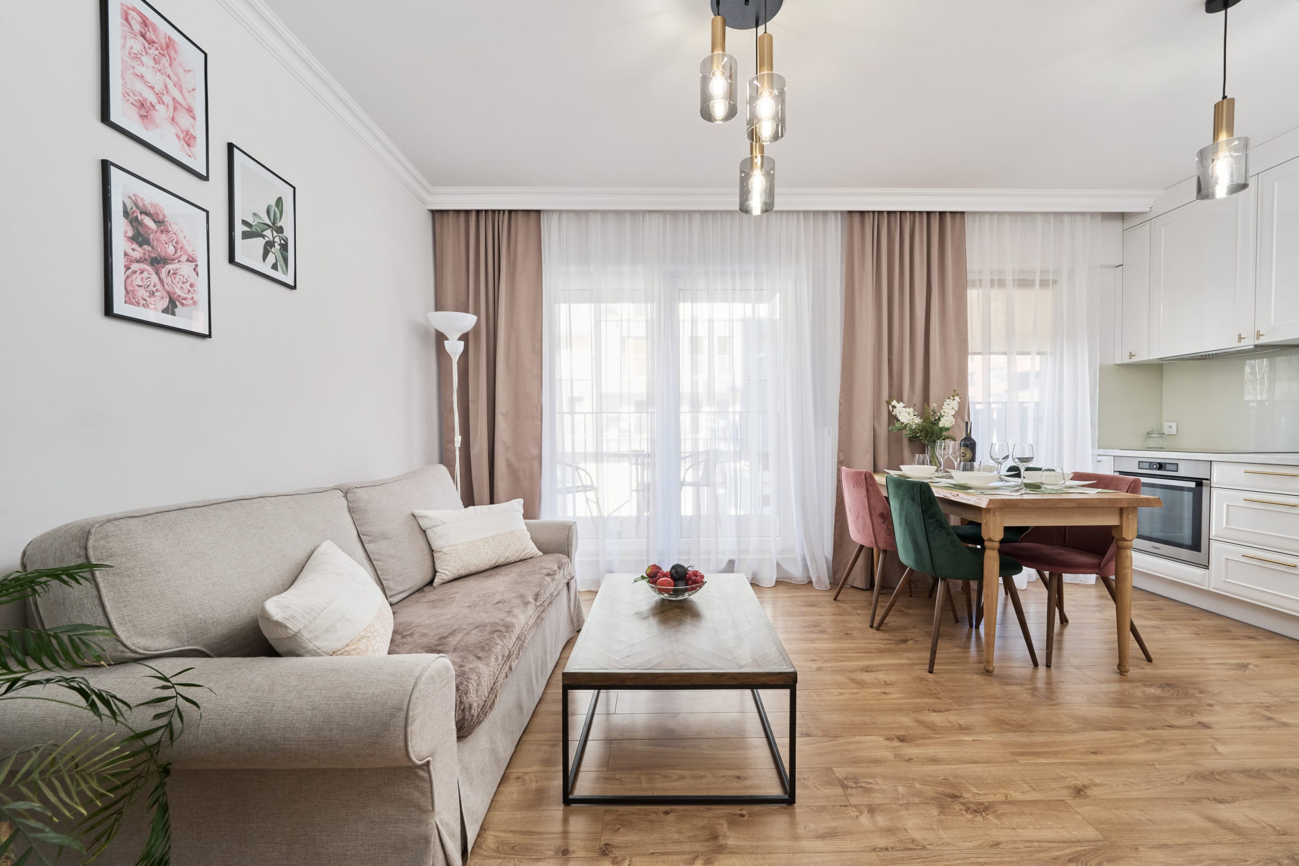 A bright living room featuring a beige sofa, a small coffee table, and a rug. Sheer curtains allow natural light to illuminate the space.