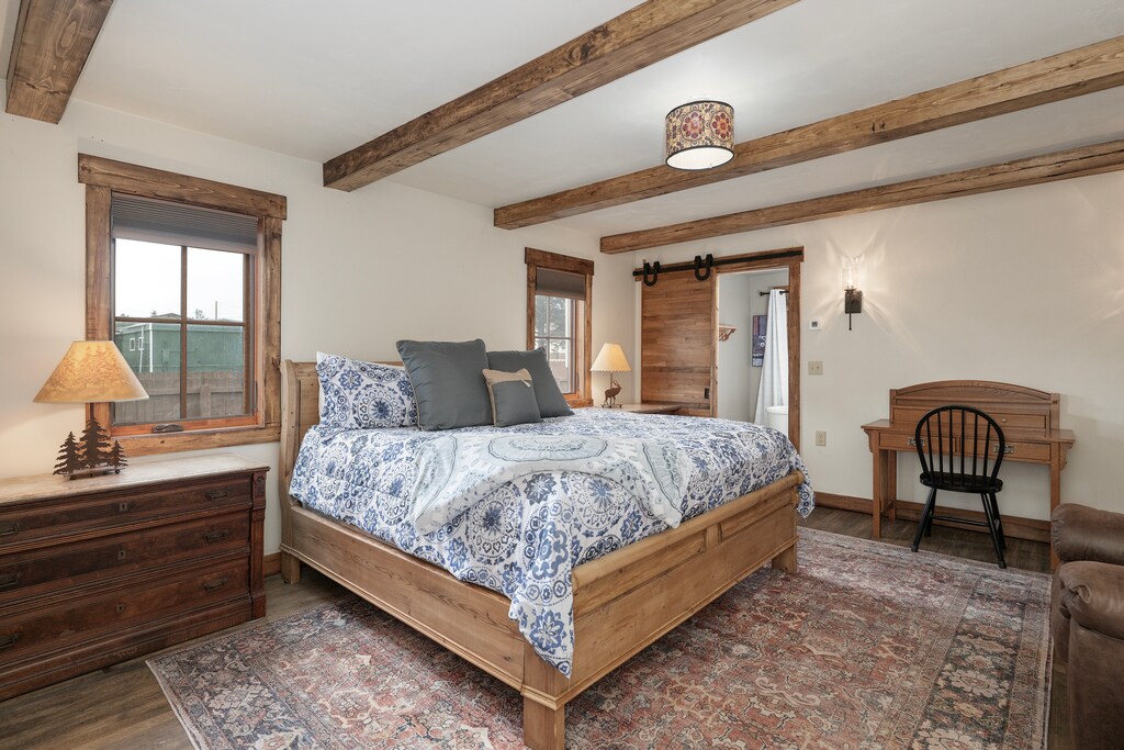 Drift off under exposed wooden beams in this cozy bedroom, where rustic charm meets comfort with quality linens and thoughtful touches.