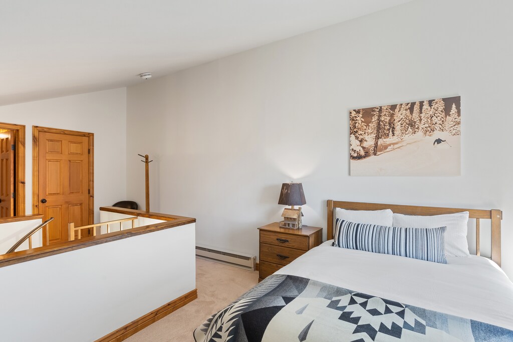 Queen sized bed with white bedding at the top of a spiral staircase. Locked off owner's closet at the top of the stairs.