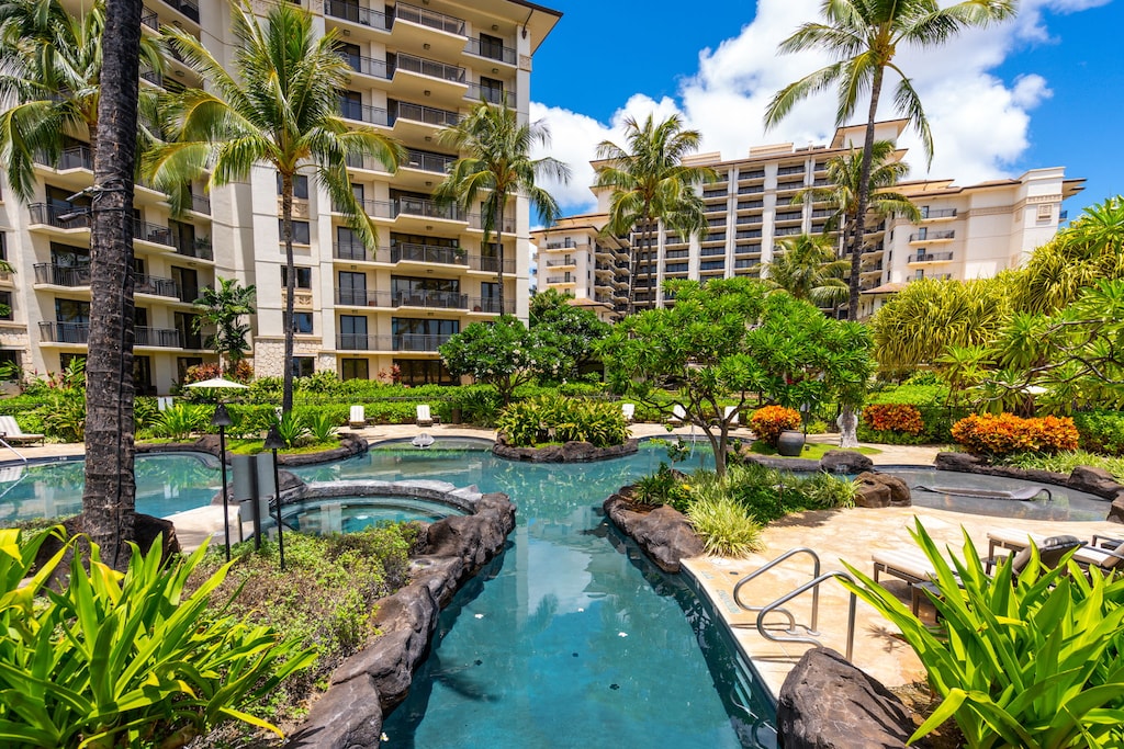 Resort-style tropical pool area surrounded by lush landscaping and towering palm trees beneath multiple high-rise buildings.