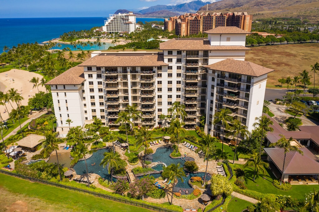 Resort complex featuring luxury towers, lagoon-style pool, and tropical landscaping near pristine beach and mountain backdrop.