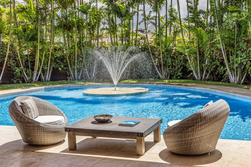 A tranquil poolside lounge area with a fountain and lush greenery creates a serene, tropical escape.