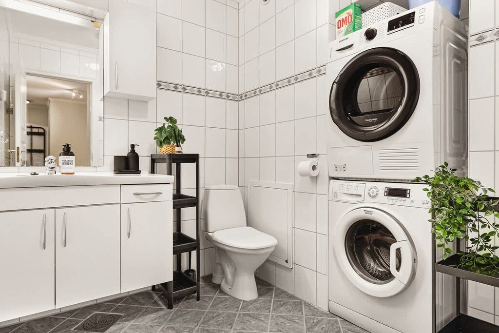 This bathroom features a spacious shower, ample storage, and a washing machine. With its bright ambiance and contemporary fixtures, it's both functional and inviting.