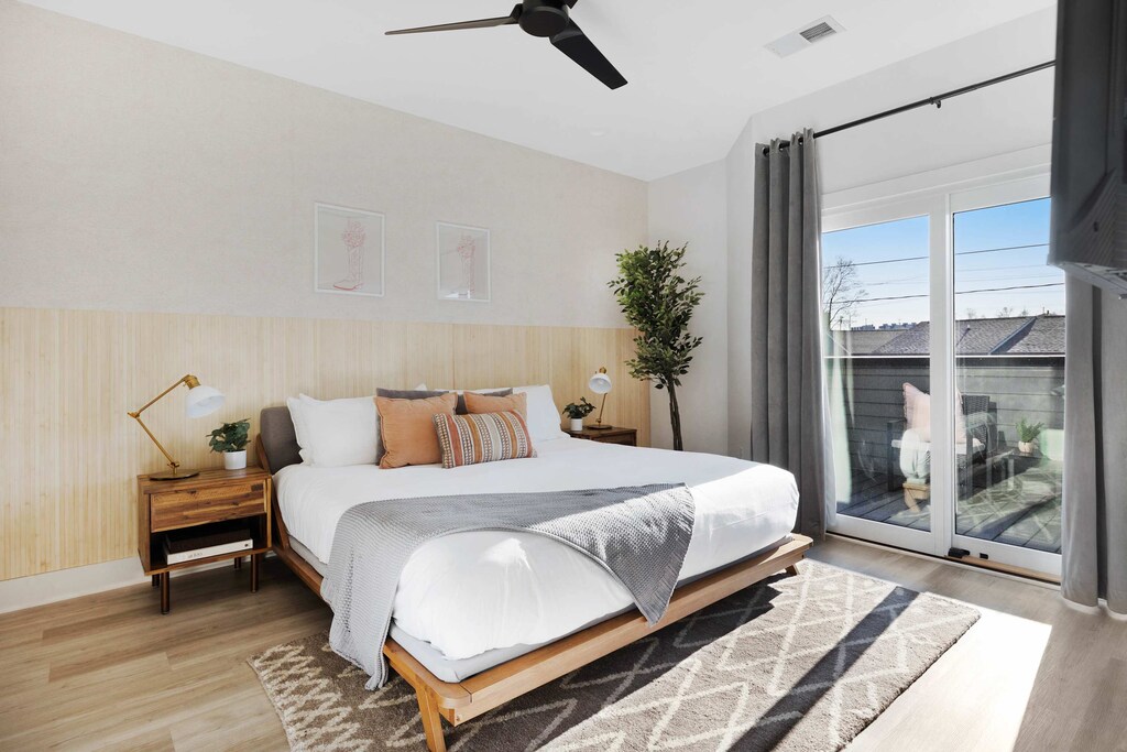 Elegant bedroom featuring a king bed, walk-in closet, and a private balcony with two chairs. Includes an en-suite bathroom with a sleek shower.