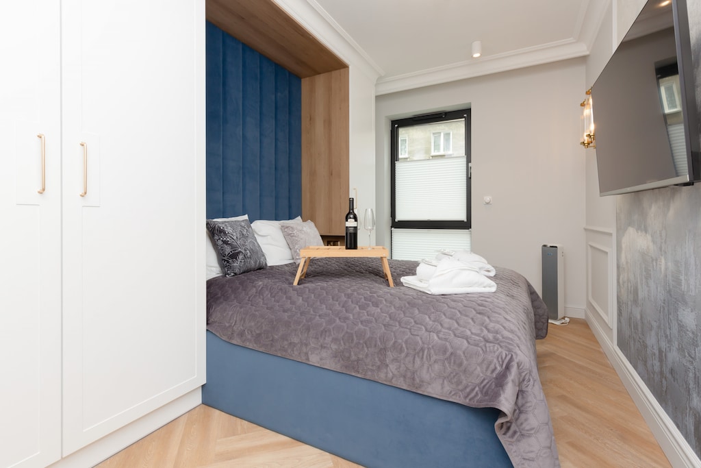 A cozy bedroom with a comfortable double bed with a gray bedspread matching the navy blue elements of the bed. Next to the bed there is a large wardrobe.