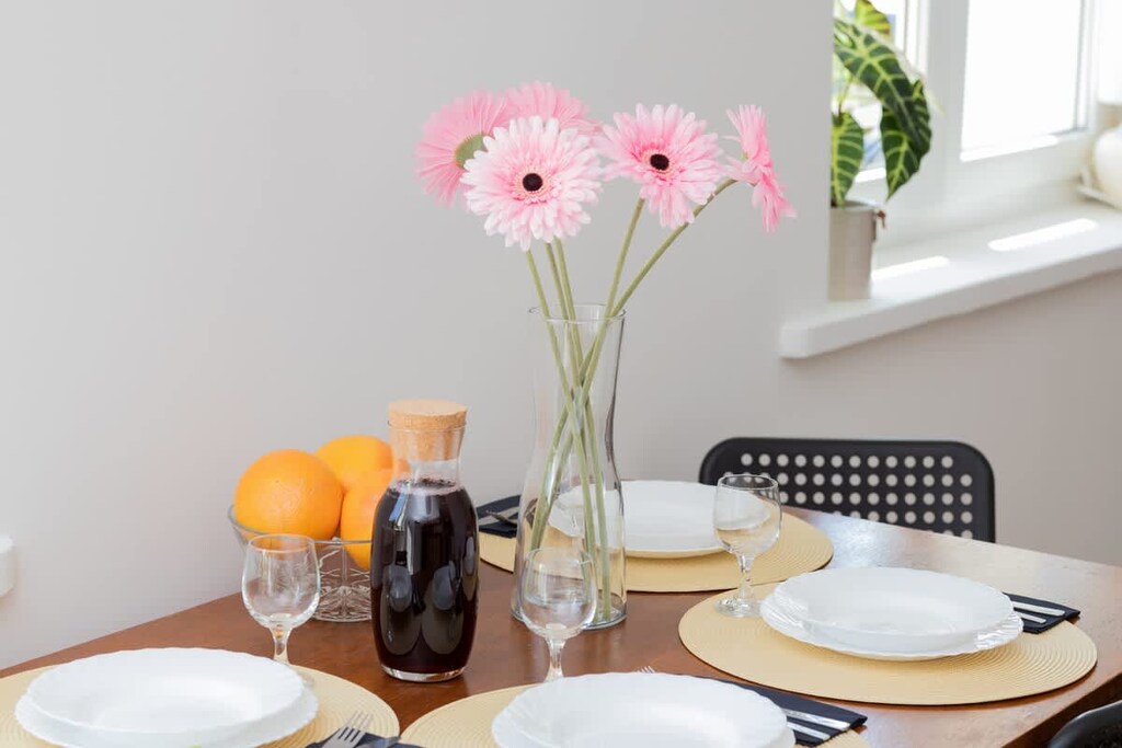 A small dining table set for two, decorated with fresh flowers, oranges, and a juice bottle for a lively atmosphere.