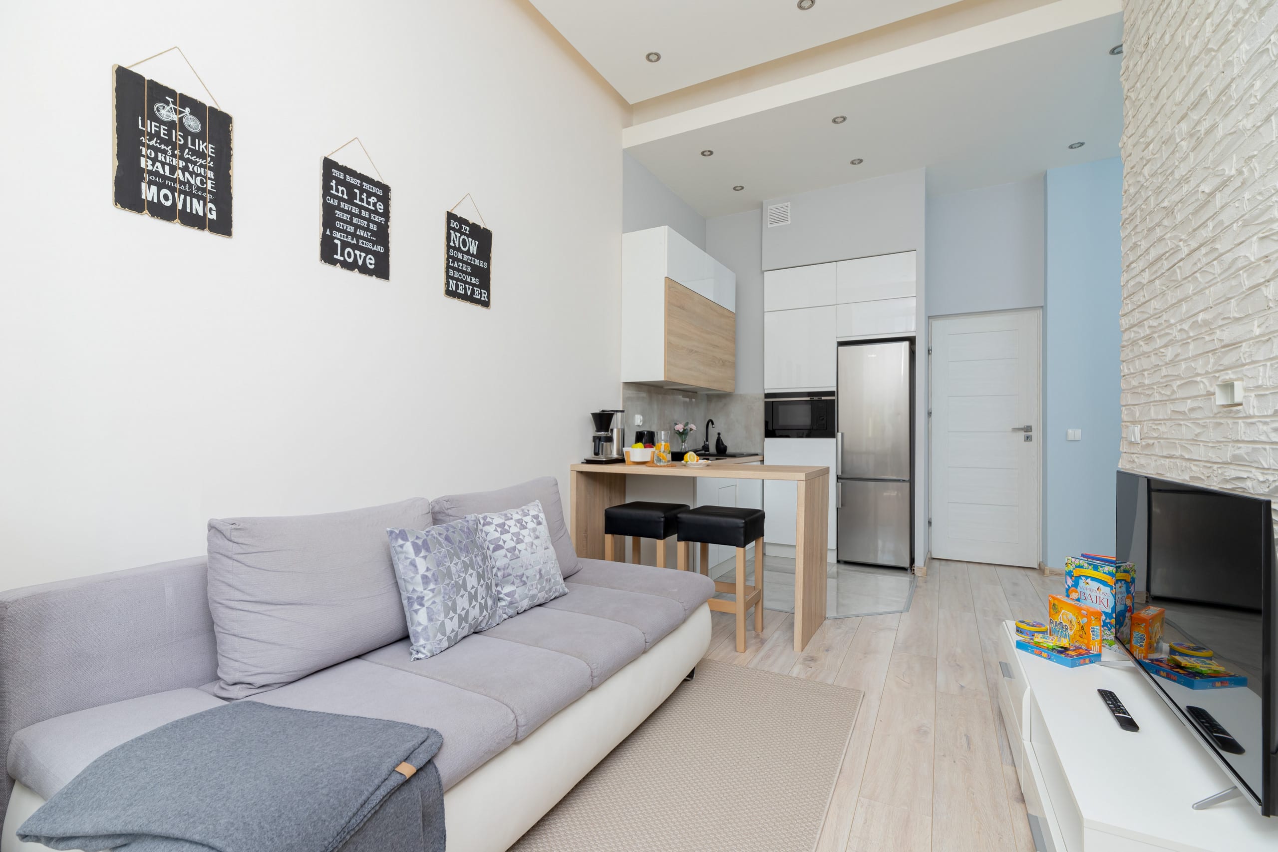 Open living area with a gray sofa, small dining table, and modern kitchen in a bright space.
