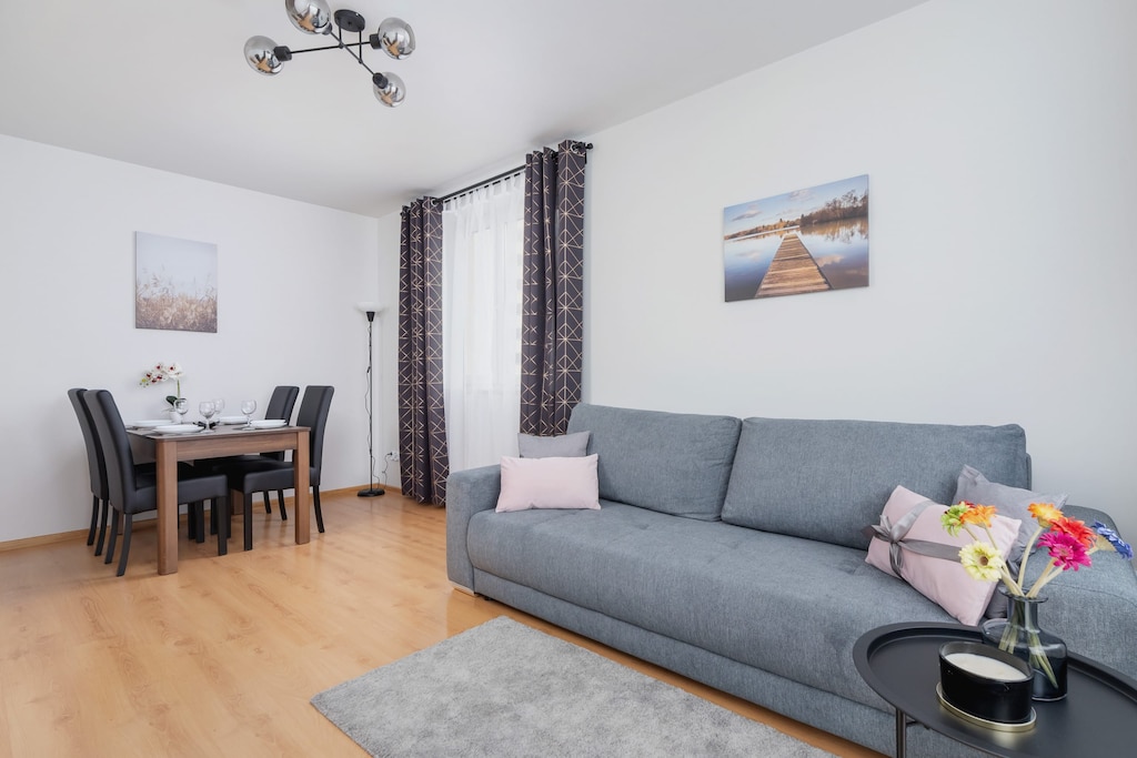 Spacious living room with dining table and chairs, light grey double sofa bed, and elegant black coffee table.