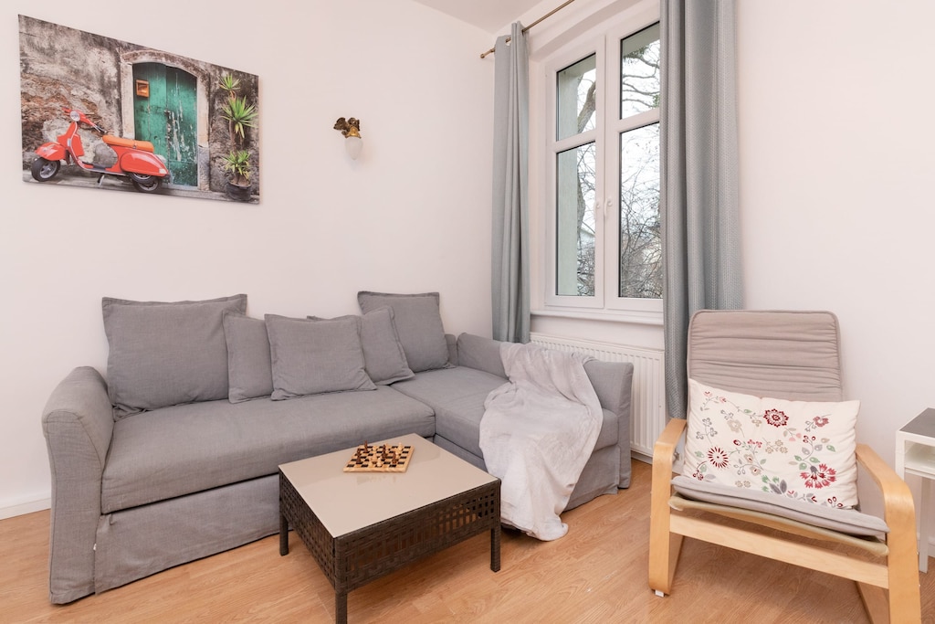 A cozy living room with a gray sofa, coffee table, and large windows letting in natural light.

