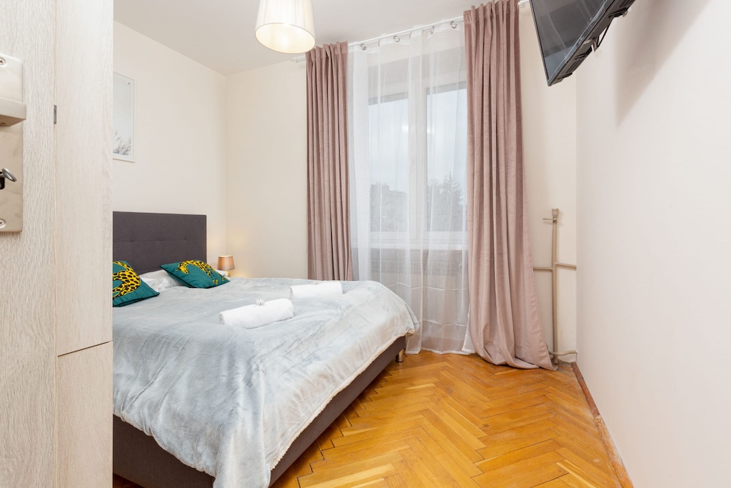 A bright bedroom with soft bedding, a large window, and minimalistic decor.
