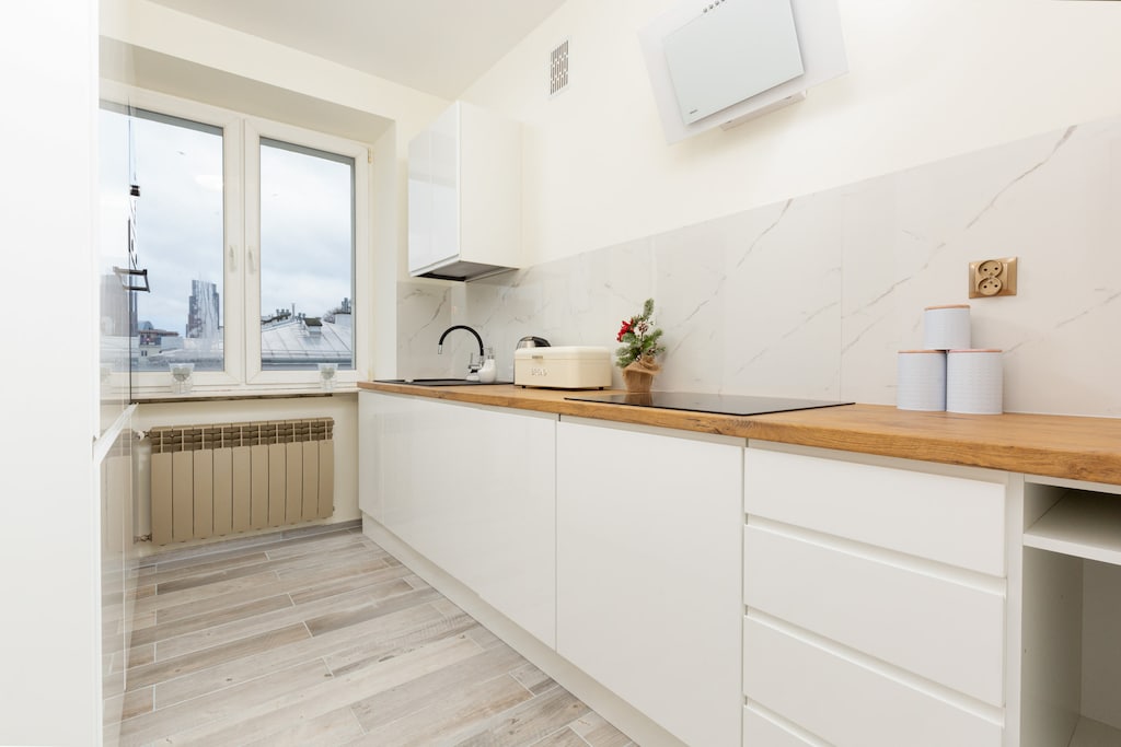 A modern kitchen with white cabinets, wooden countertops, and a large window.
