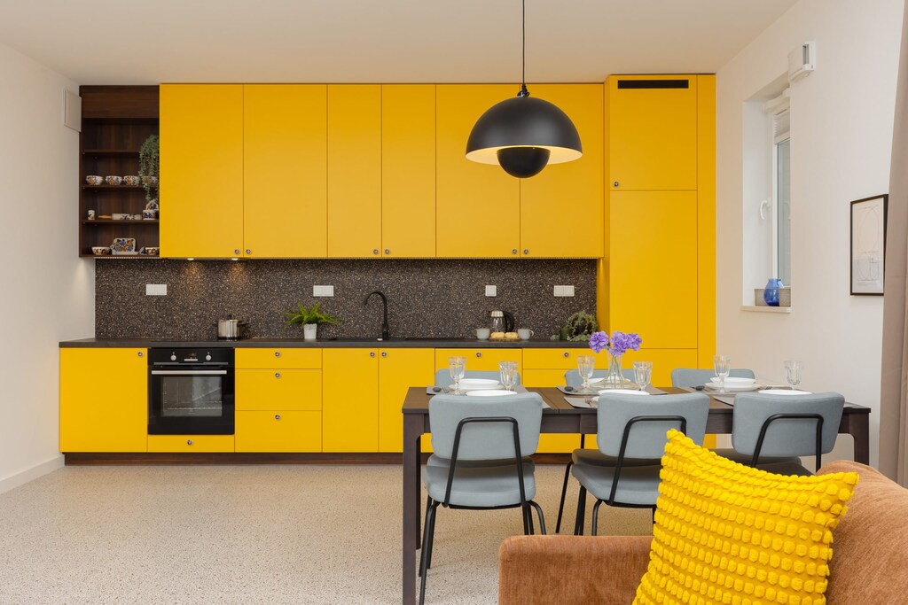 Fully equipped kitchen with vibrant yellow cabinets, a dining table, and modern appliances, ideal for meal preparation.
