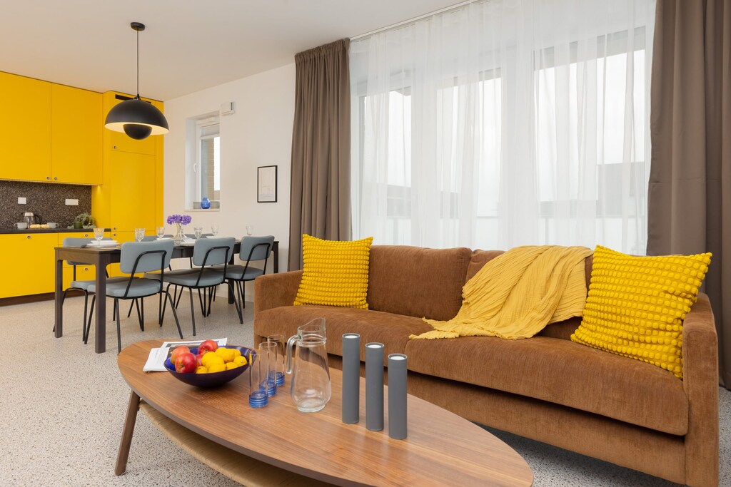 Bright living room with a cozy sofa, yellow cushions, and a stylish wooden coffee table, creating a warm and inviting atmosphere.
