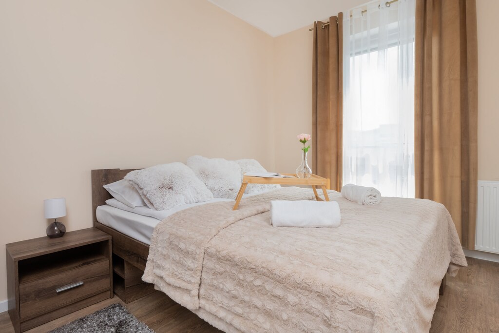 A well-lit bedroom with a neatly made bed, soft beige bedding, and a serene atmosphere.