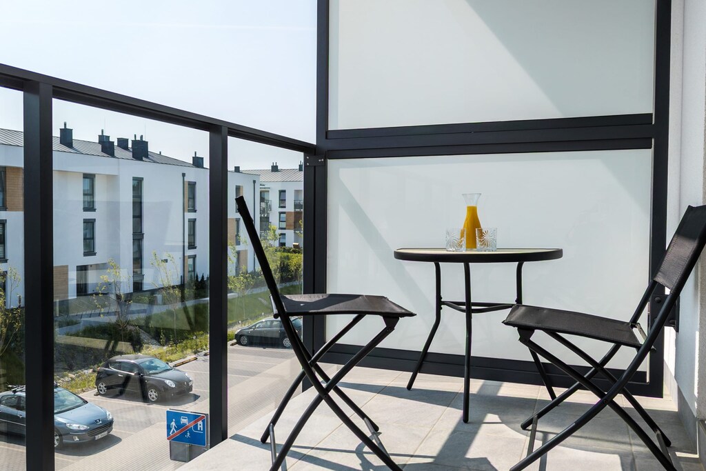 A small balcony with modern outdoor seating, offering a view of the residential complex.