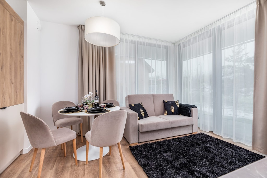 A bright, cosy living room space where the seating area is combined with the dining area. A decorative black carpet lies on the floor.