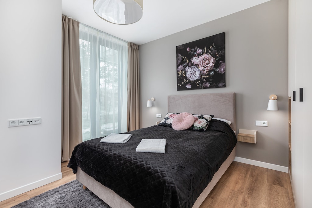 Modern bedroom with double bed with black bedspread. On the wall hangs a painting depicting flowers on a black background.