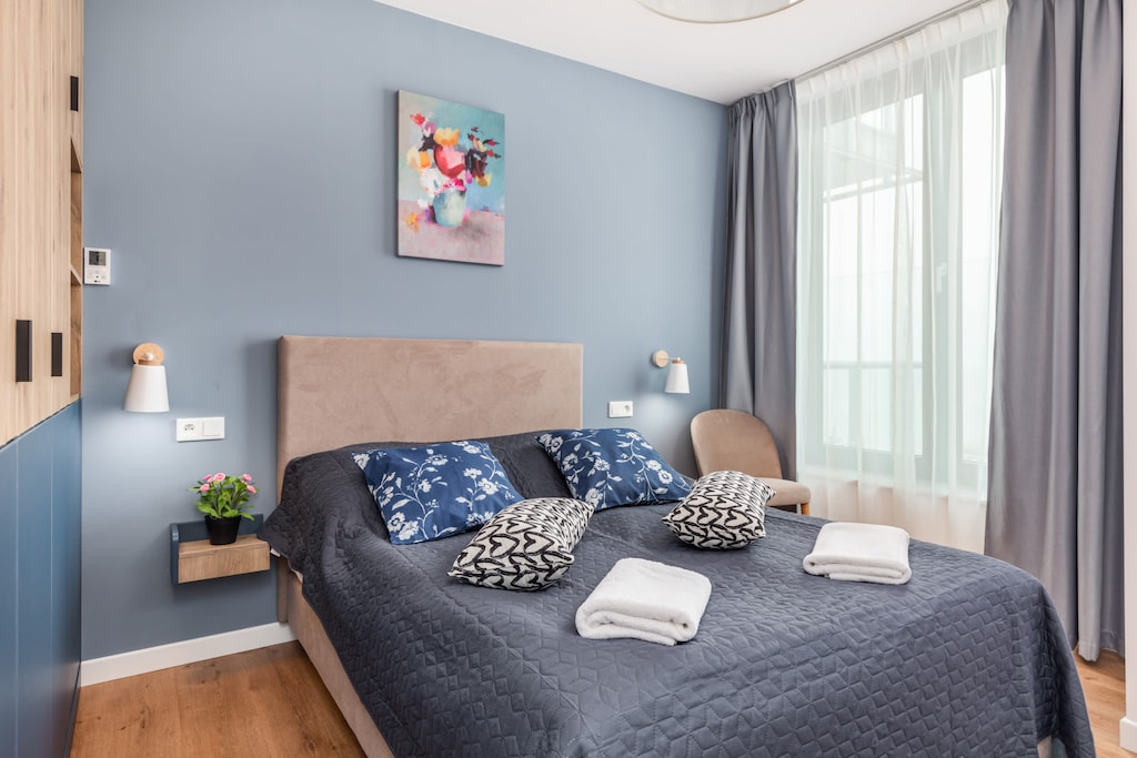 A neatly arranged bedroom with a double bed, blue bedding, and light curtains, offering a relaxing vibe.