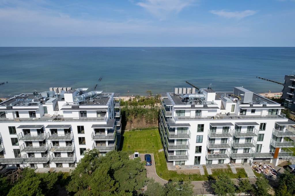 An elevated perspective showing modern apartment buildings surrounded by greenery, with the sea in the background.