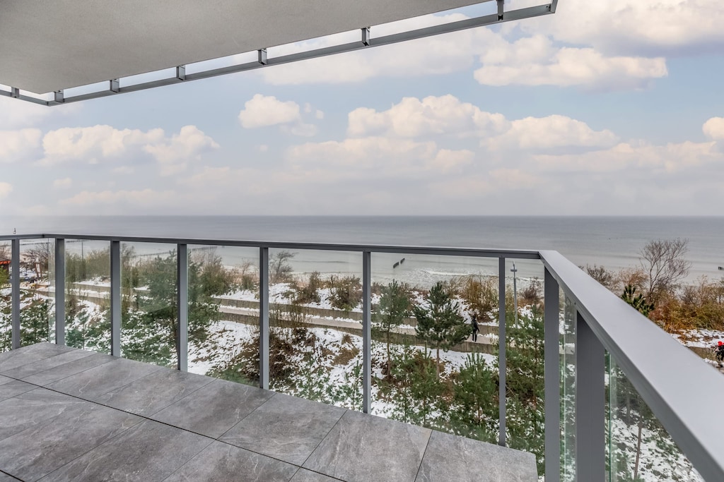 A balcony with a glass railing offering a stunning view of the beach and the sea.