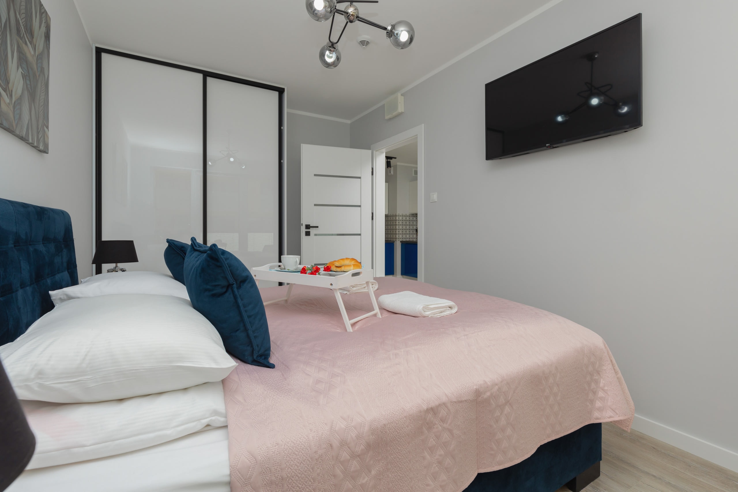 A bedroom featuring a pink bed, dark blue couch, and a mirrored wardrobe. This provides plenty of storage space.