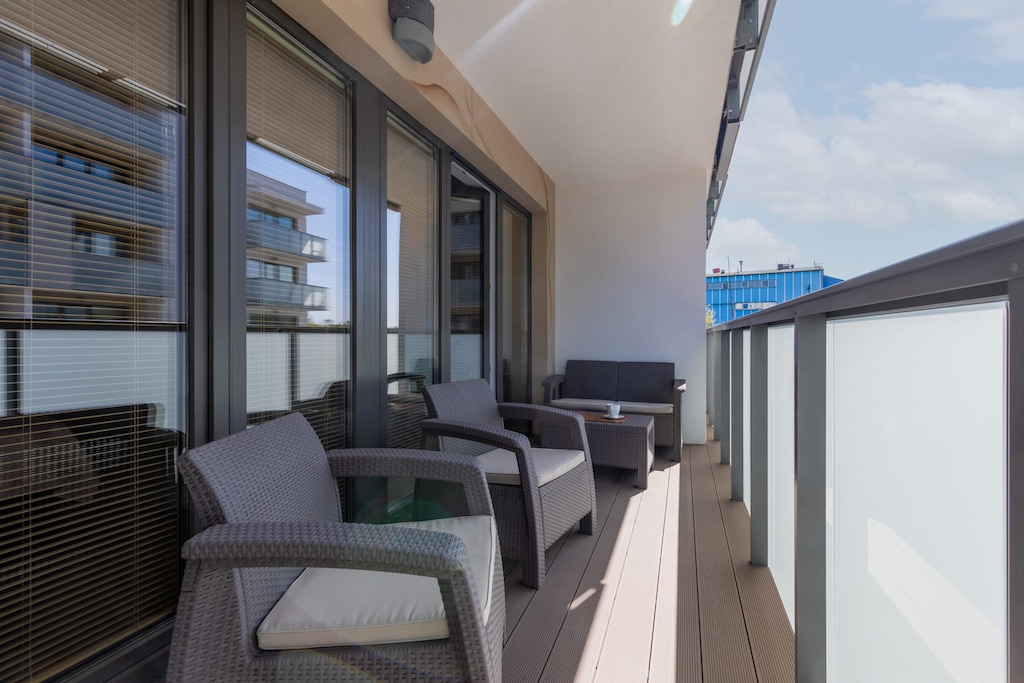  A balcony with a table and two chairs, overlooking other buildings. The area looks bright and sunny.