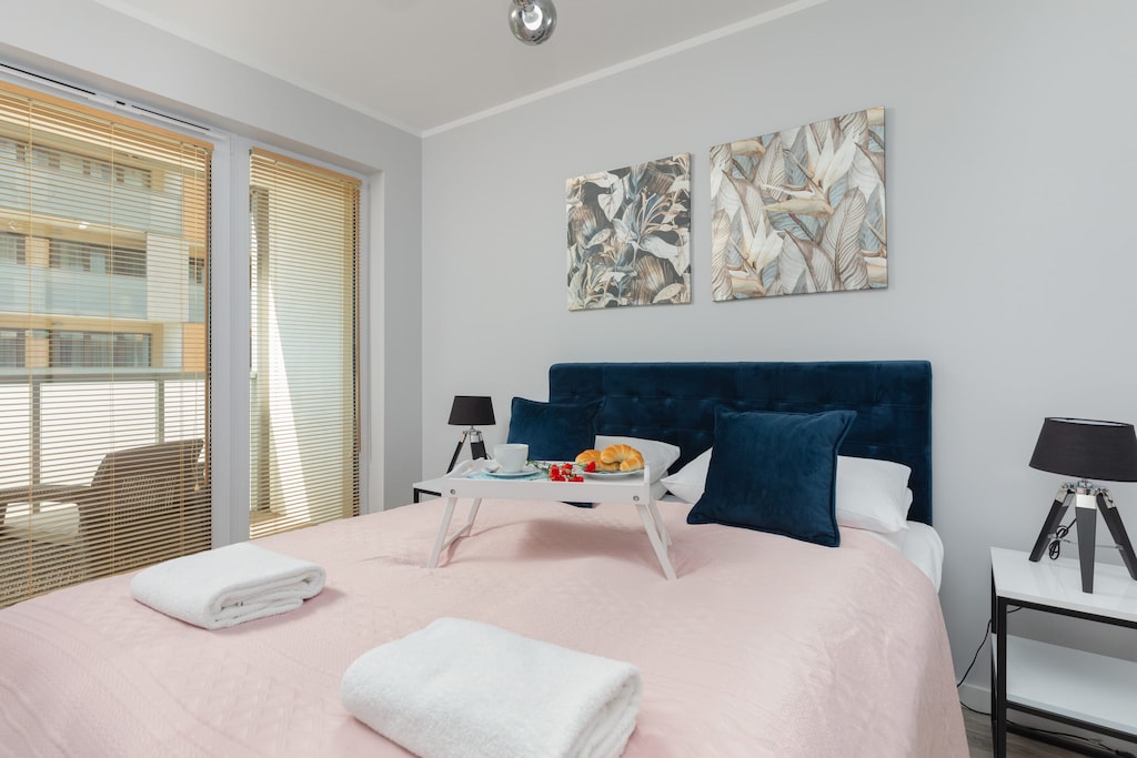 A bedroom featuring a queen-size bed with pink bedding, a small bedside table with a lamp, and a mirrored wardrobe.