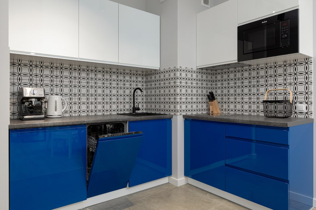 A modern kitchen with blue lower cabinets, white upper cabinets, and a patterned backsplash. The space is clean and well-lit.