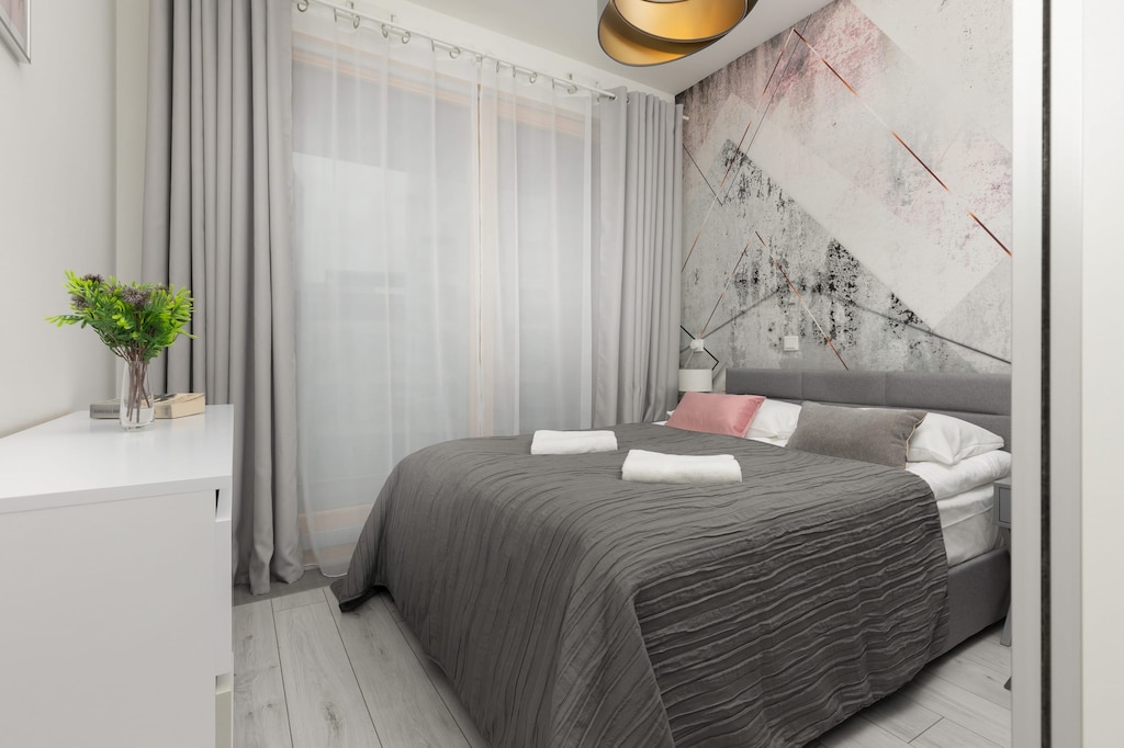 A cozy bedroom with a double bed, gray bedding, and a patterned accent wall.
