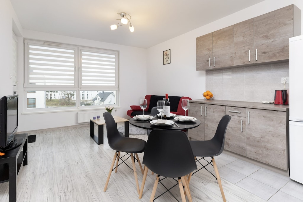 A modern and open living space featuring a red sofa, a sleek coffee table, and a dining table set for two, blending functionality and style.