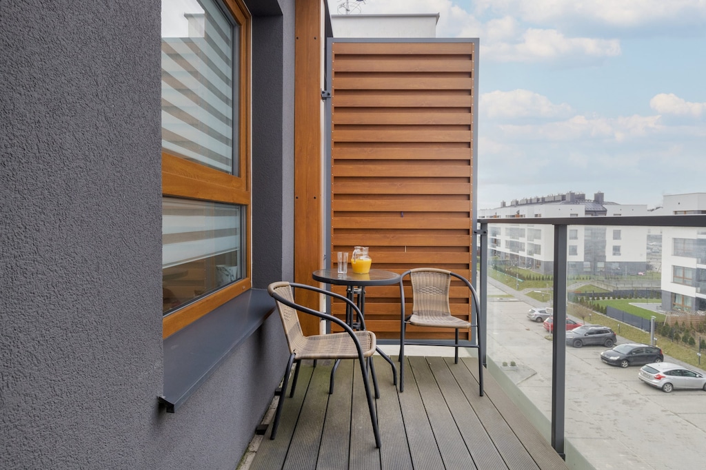 A private balcony with a small table and chairs, overlooking a modern residential area with plenty of natural light.