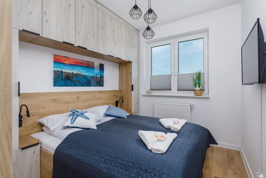 A bedroom with a comfortable double bed, wooden accents, and a window providing a bright, airy ambiance.
