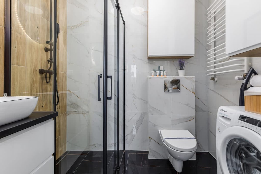 A sleek bathroom with marble-style tiles, a walk-in shower, and a washing machine for convenience.
