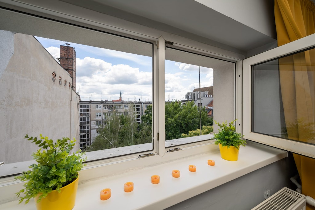 A cozy window nook with potted plants, large windows, and a view of the surrounding buildings.