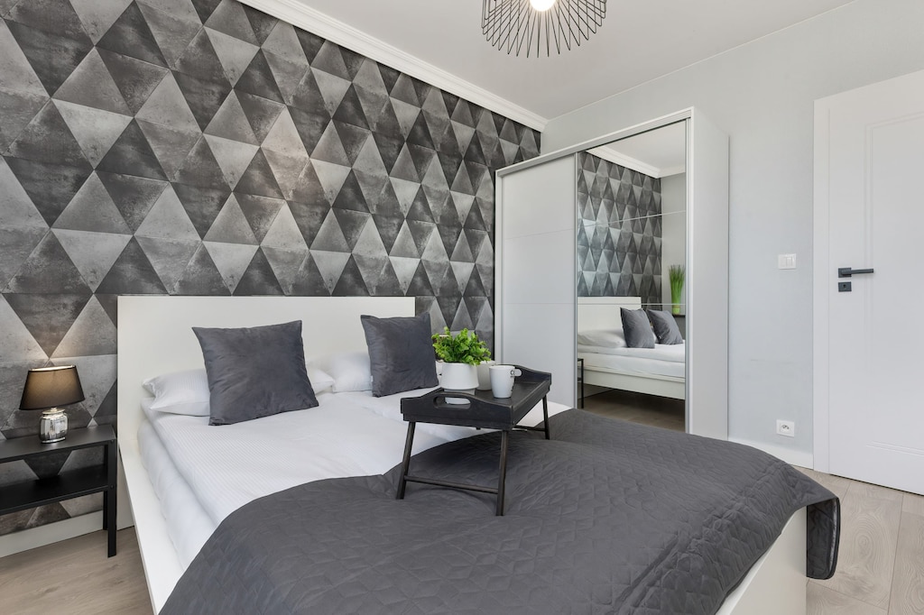 A stylish bedroom with a double bed, gray bedding, and a geometric accent wall, creating a modern and comfortable ambiance.
