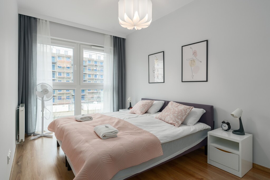 A bright bedroom featuring a double bed with pink bedding and framed wall art.

