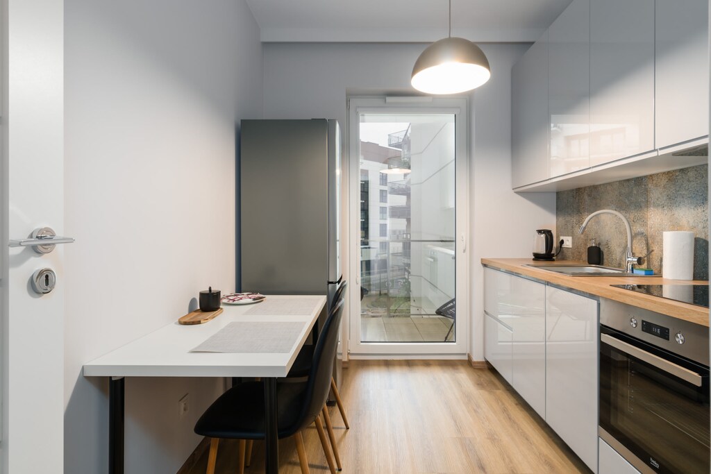 A modern kitchenette with a wooden countertop, white cabinets, and a dining area with a small table.
