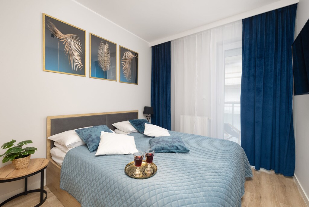 A cozy bedroom with a comfortable double bed with a visible blue bedspread, and matching blue curtains in the windows, which give the room a touch of lightness.