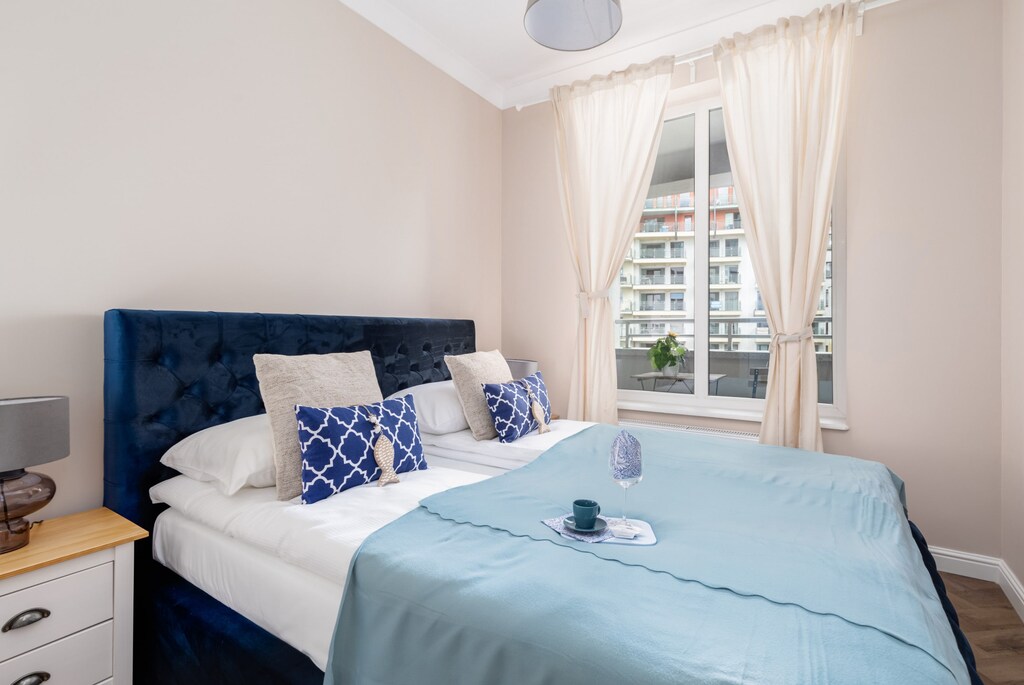 A bright bedroom with a comfortable blue bed, soft pillows, and elegant curtains.

