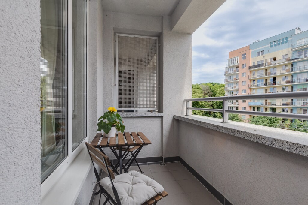 A balcony with a small table, chairs, and a pleasant view of the surrounding buildings and greenery.

