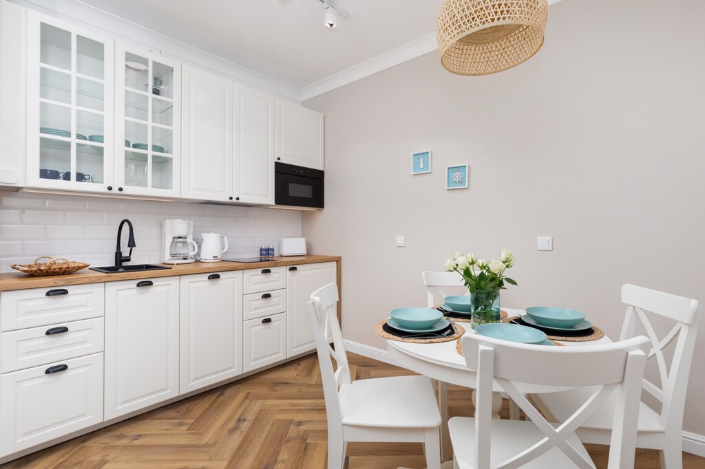A modern kitchen with white cabinets, wooden countertops, and a dining table set for two.

