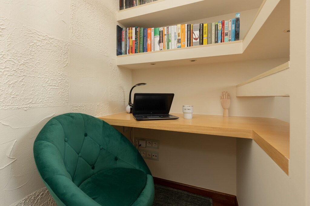 A small workspace with a wooden desk, shelves, and a comfortable green chair.

